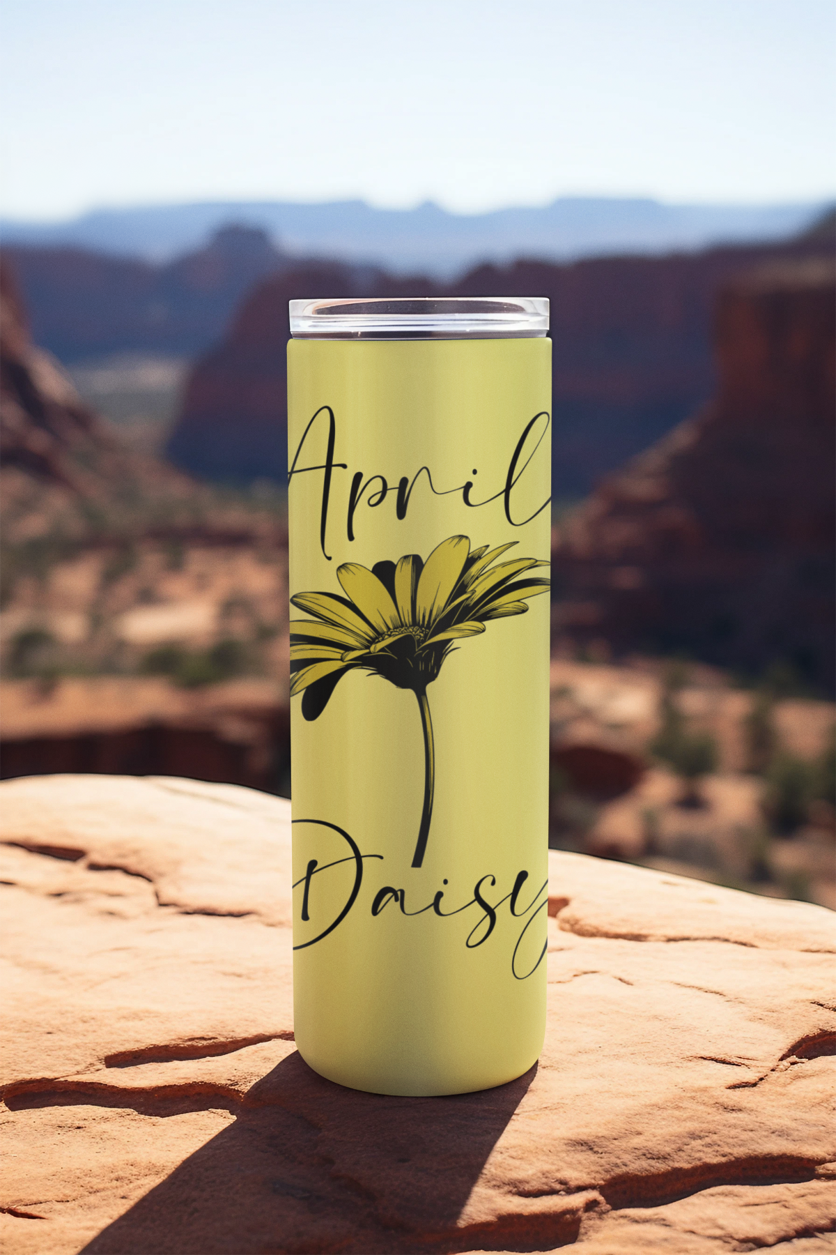 April daisy tumbler from Monthly Floral Bloom Collection sitting on rock with scenic canyon view