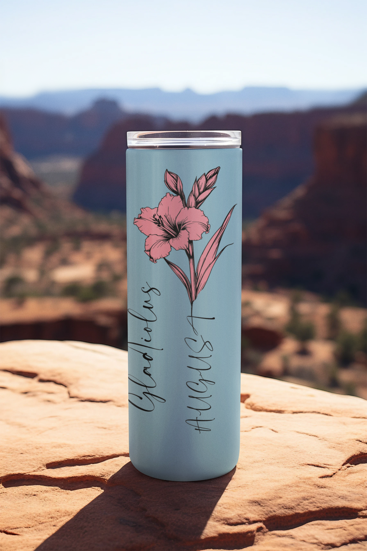 Pink flower August tumbler on rocky ledge with desert mountain background