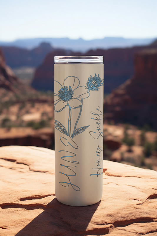 20oz ivory tumbler with blue honeysuckle flower and June script, displayed outdoors on a canyon rock