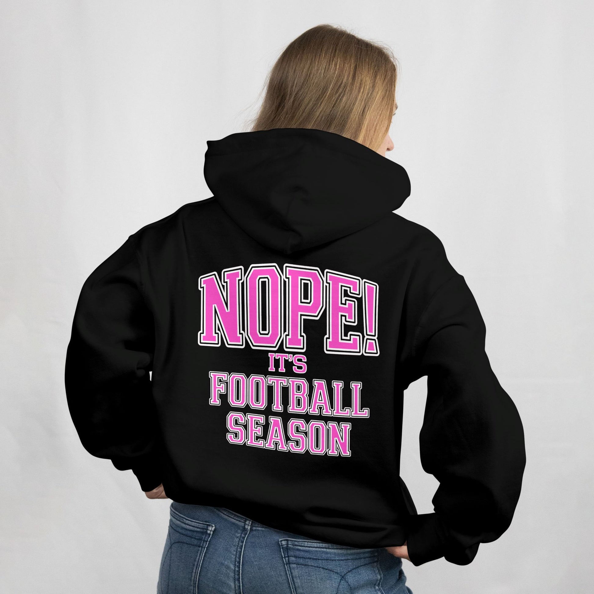 Person wearing a black hoodie with pink text on the back, standing against a plain background