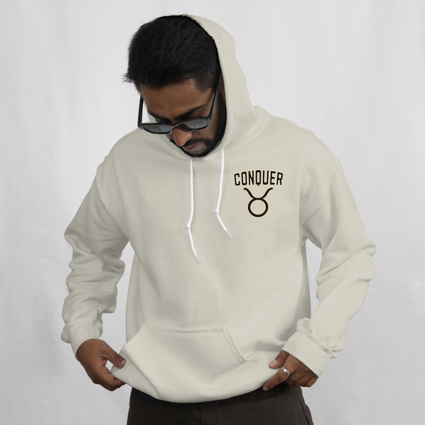 Man wearing a beige hoodie with 'CONQUER' logo on a white background