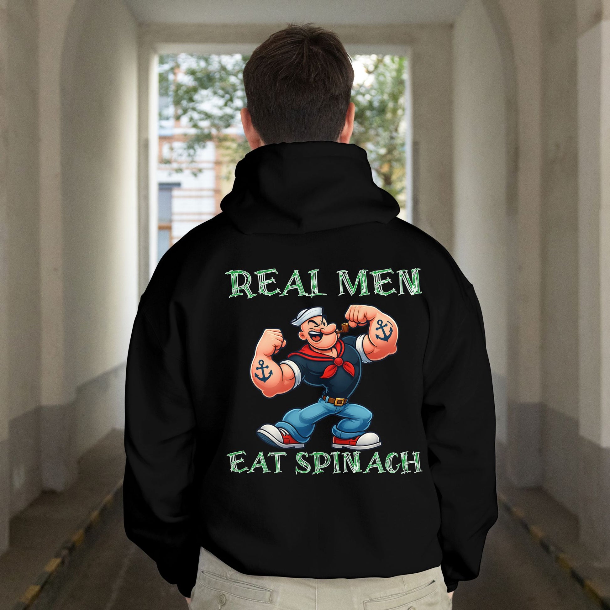 Person wearing a black hoodie with a cartoon character and text on the back, standing in a hallway.