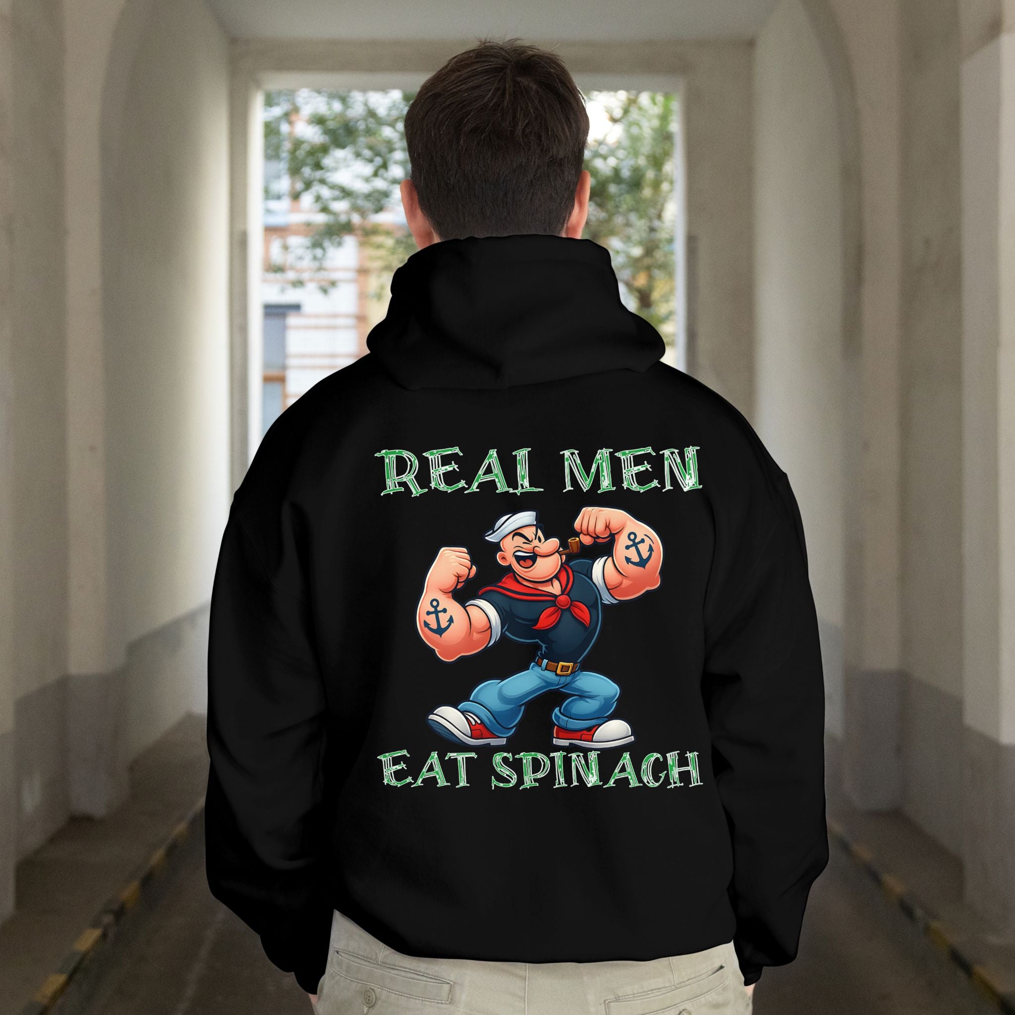 Person wearing a black hoodie with a cartoon character and text on the back, standing in a hallway.