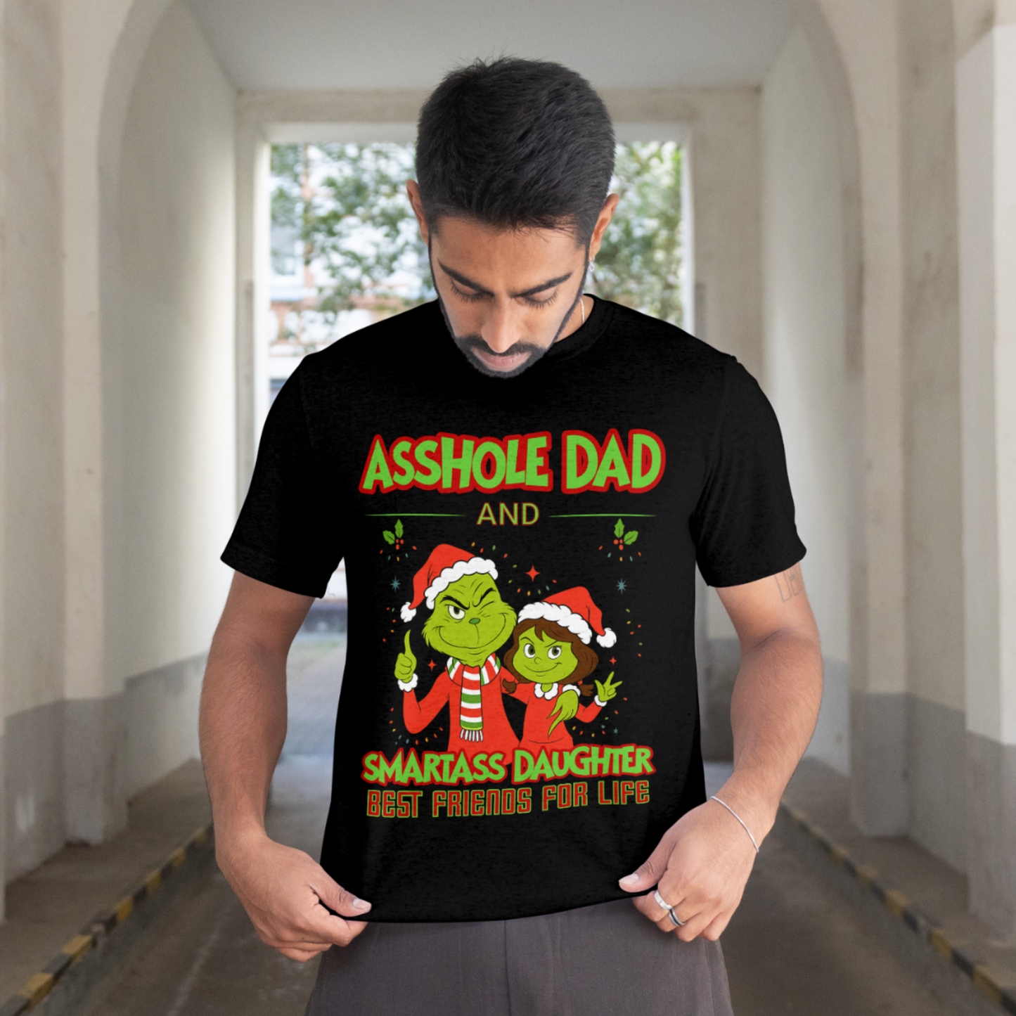 Man wearing black Christmas graphic tee that says “Asshole Dad and Smartass Daughter Best Friends for Life” with two green cartoon characters in Santa hats