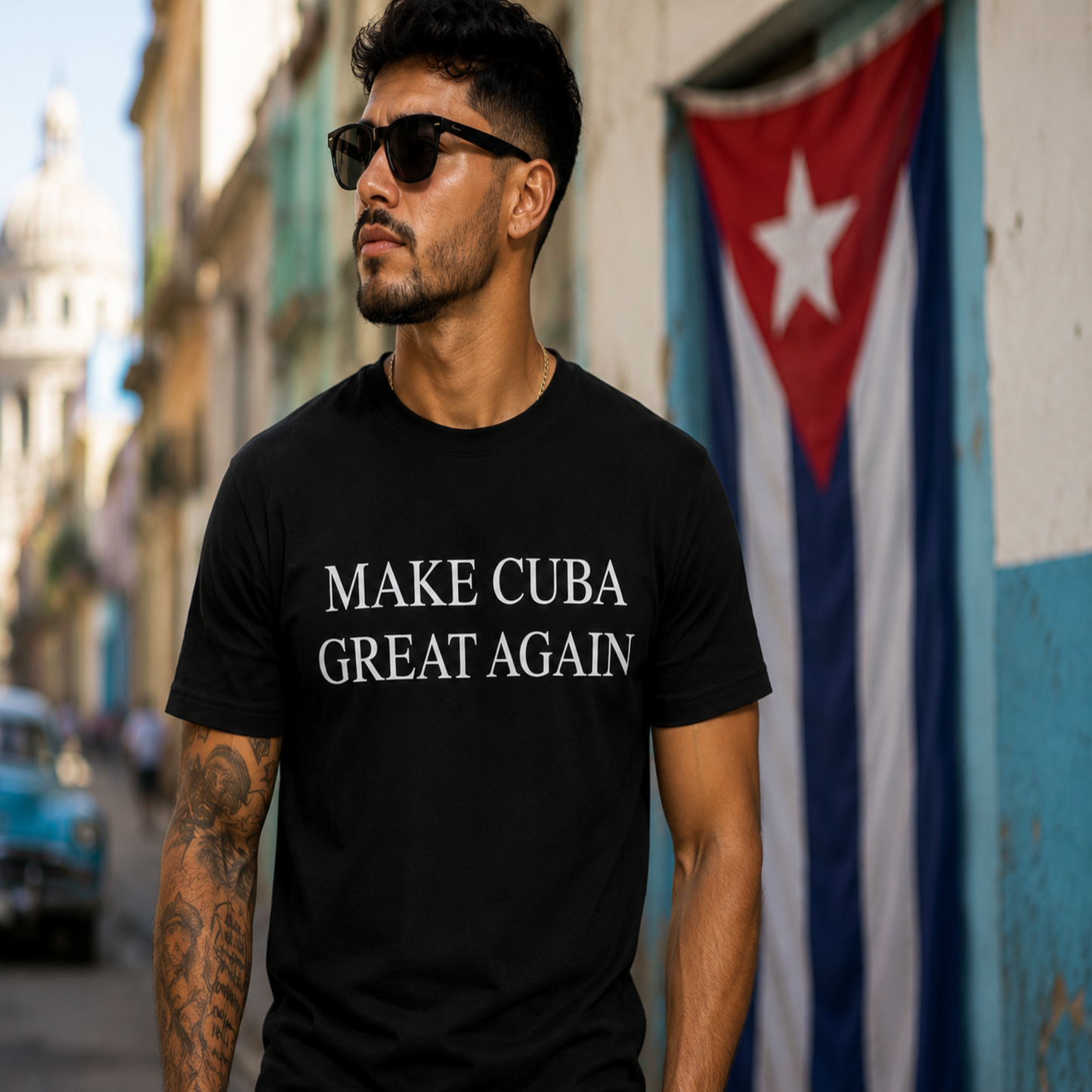 A man wearing a black t-shirt with the text 'MAKE CUBA GREAT AGAIN' in white capital letters, standing outdoors in front of a Cuban flag.