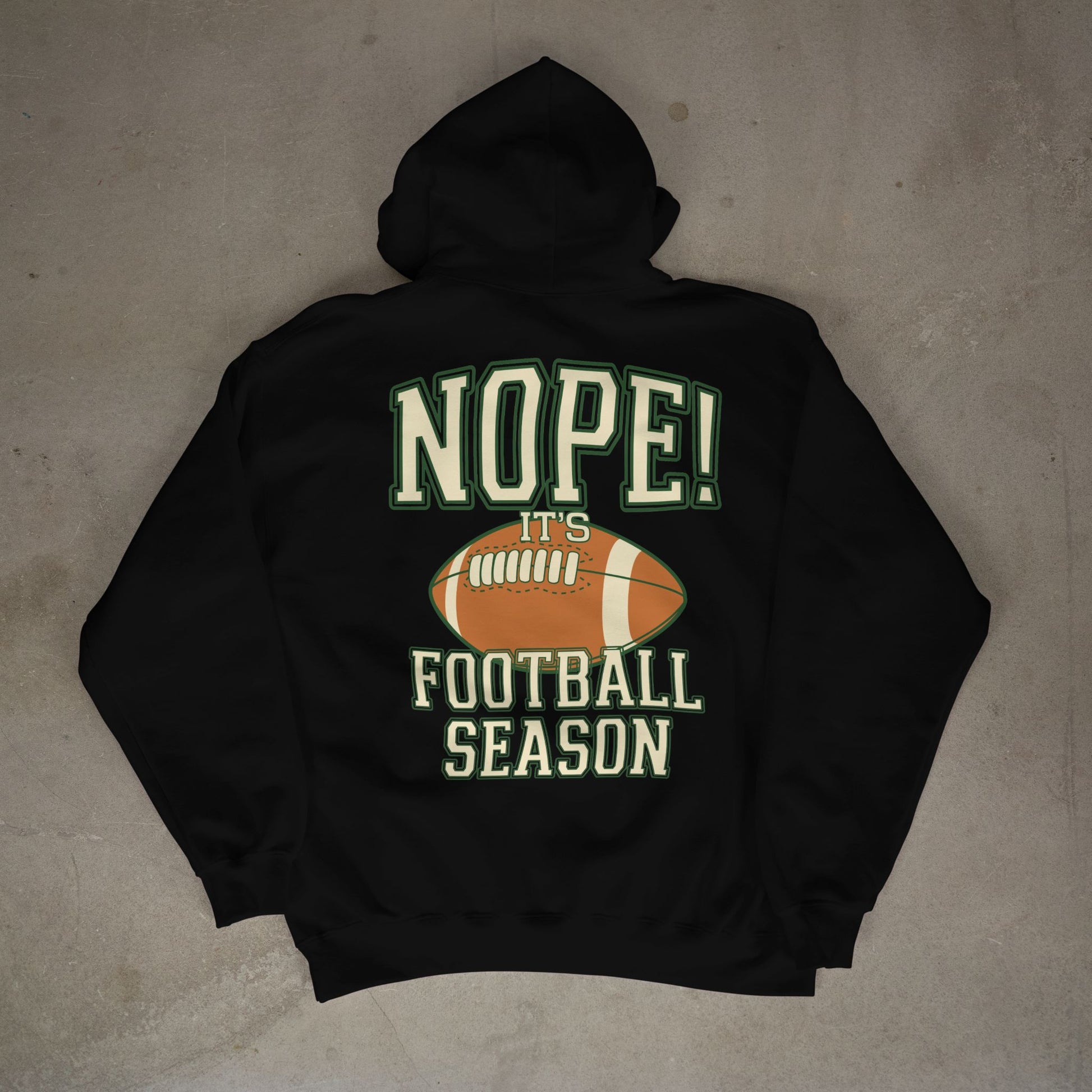 Black hoodie with 'NOPE! It's Football Season' text and football graphic on a concrete floor.