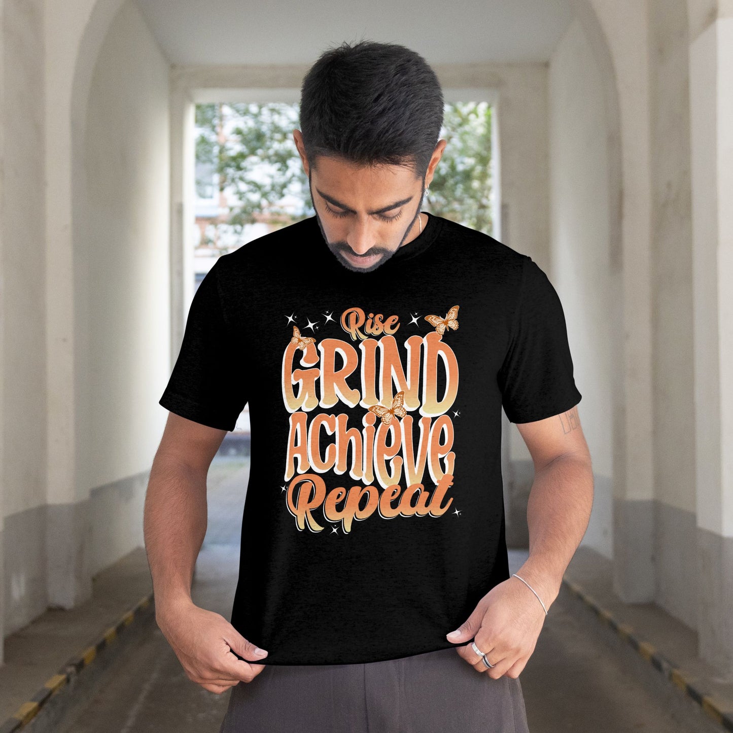 Man wearing a black t-shirt with 'Rise Grind Achieve Repeat' text in an urban setting